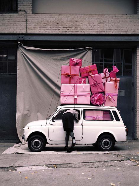 a man standing next to a white car with a pile of presents on top of