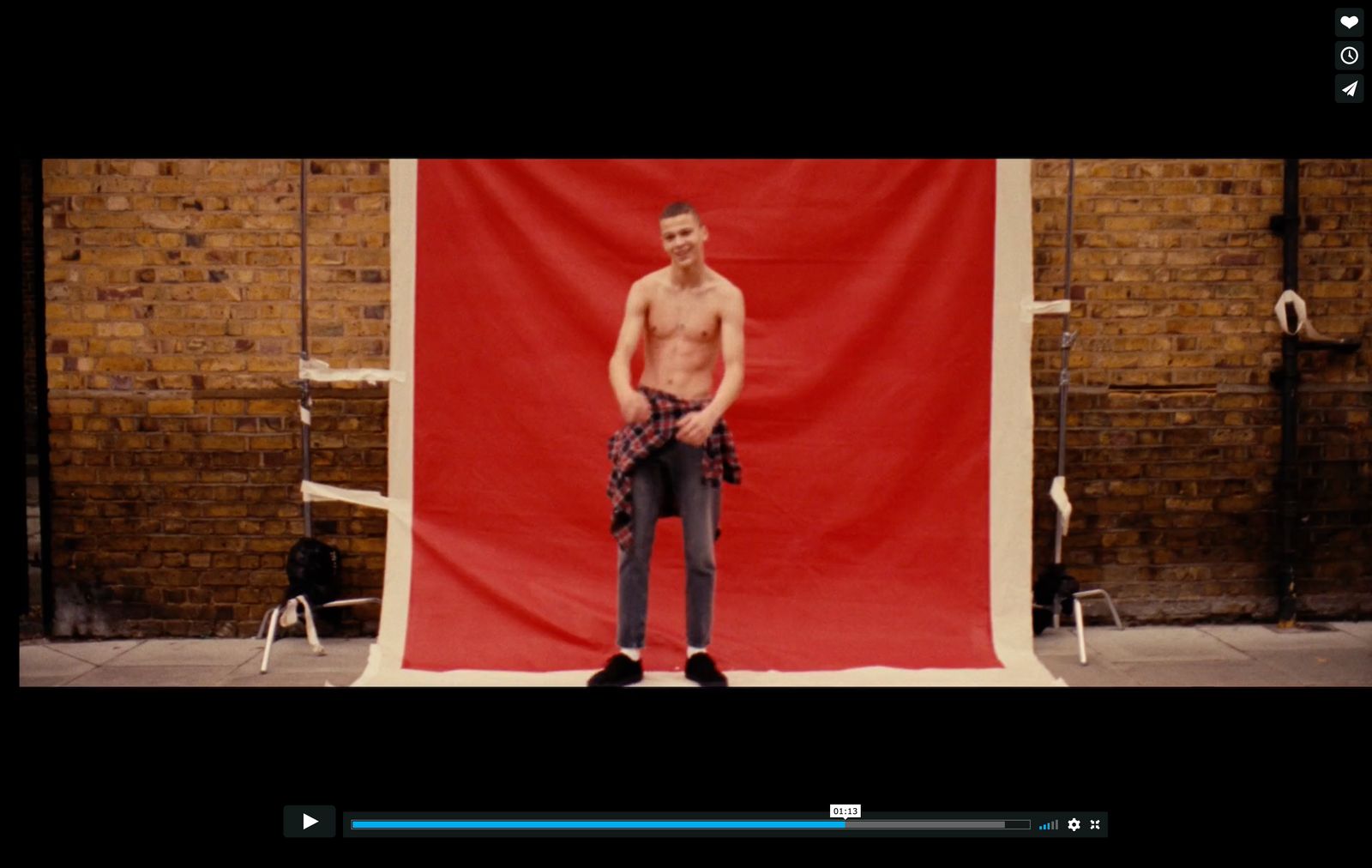 a shirtless man standing in front of a red backdrop