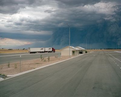 a truck is driving down the road in front of a large cloud