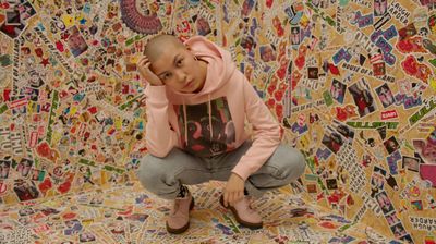 a young girl sitting on the ground in front of a wall covered in stickers