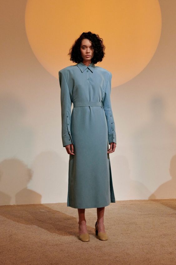 a woman in a blue dress standing in front of a wall