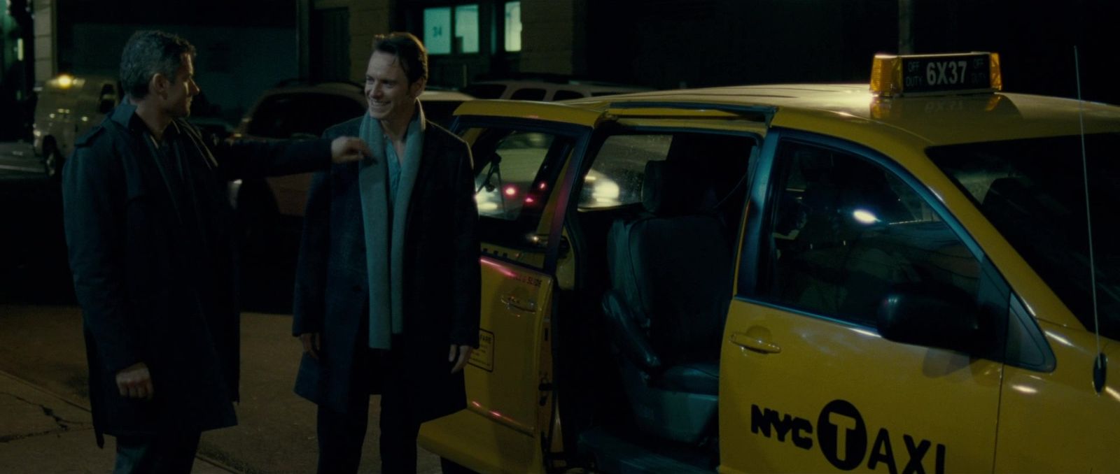 two men standing next to a taxi at night