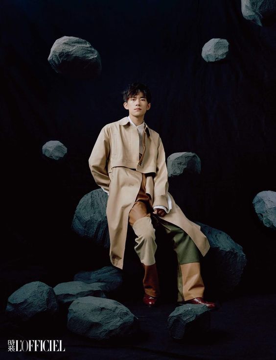 a man in a trench coat sitting on a rock