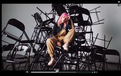 a woman with pink hair sitting on a stack of chairs