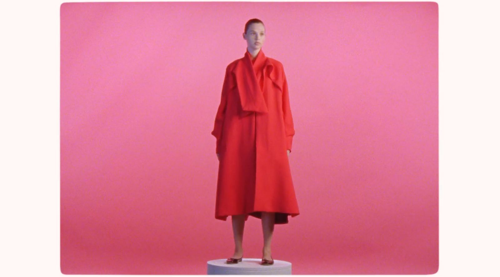 a mannequin dressed in a red coat stands in front of a pink background