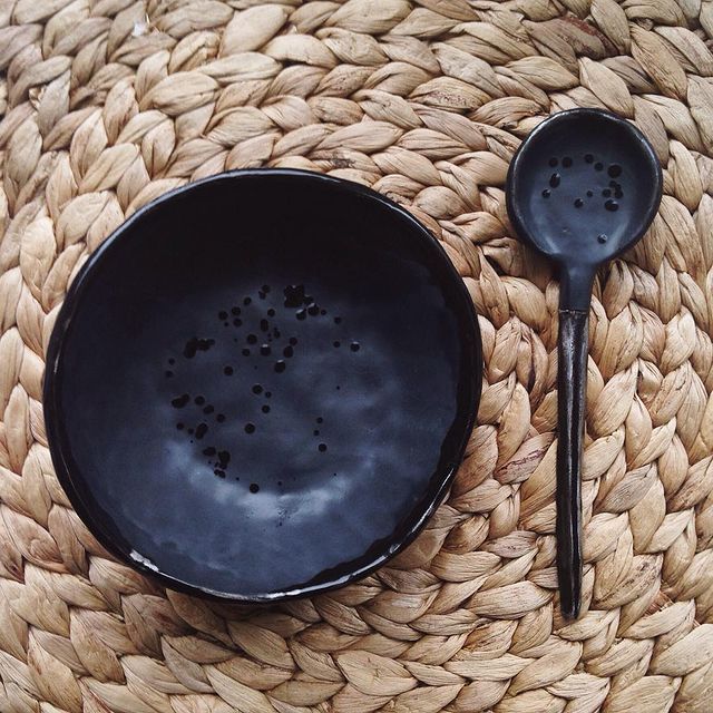 a black bowl and two black spoons on a woven mat