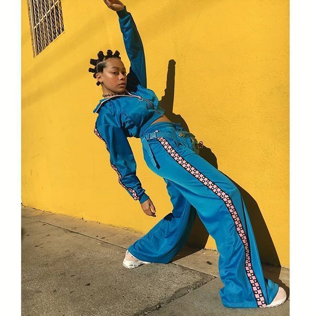 a woman in a blue jumpsuit leaning against a yellow wall