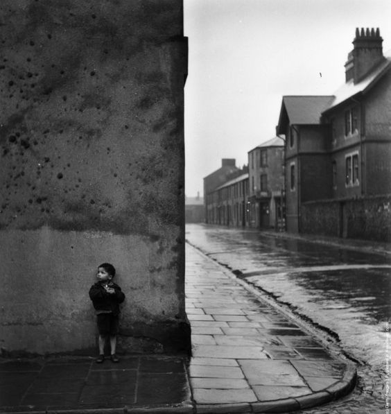 a little boy standing next to a building on a wet street