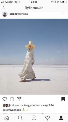 a woman in a white dress and hat walking across a field