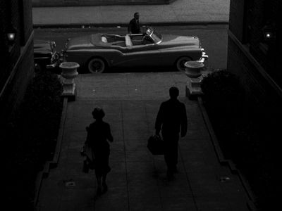 a couple of people walking down a sidewalk next to a car