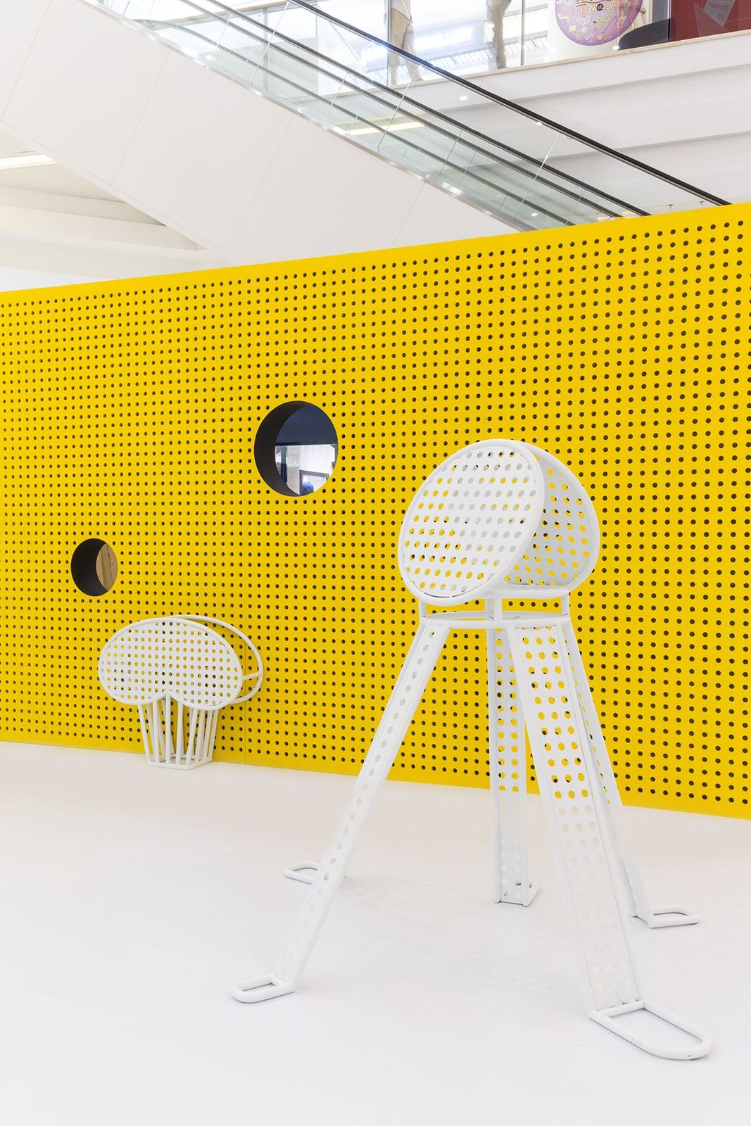 a yellow wall with two white chairs and a mirror