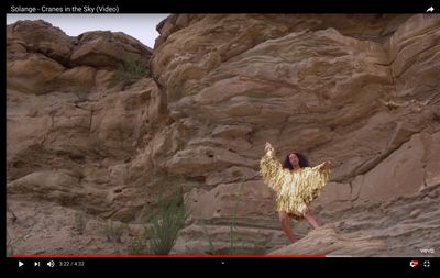 a woman in a gold dress standing in front of a rock formation