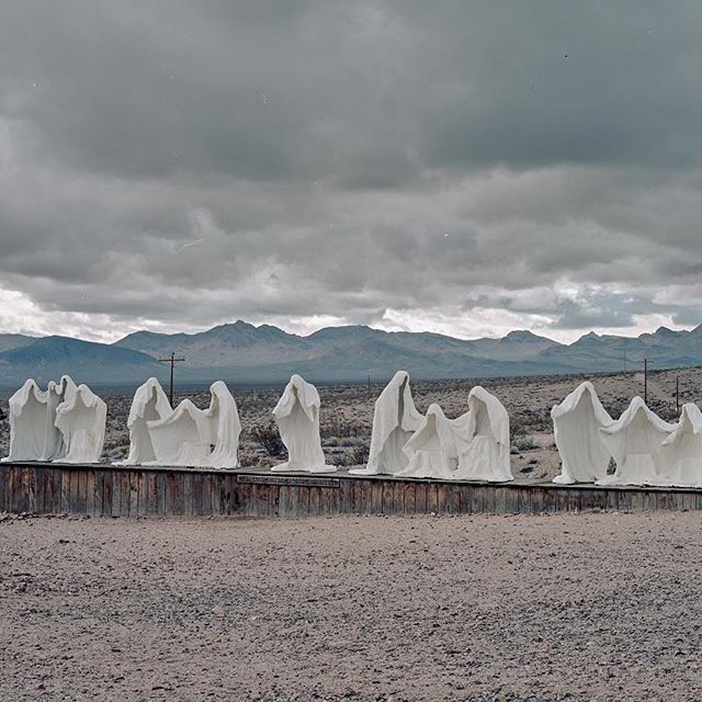 a row of white sculptures sitting on top of a dirt field