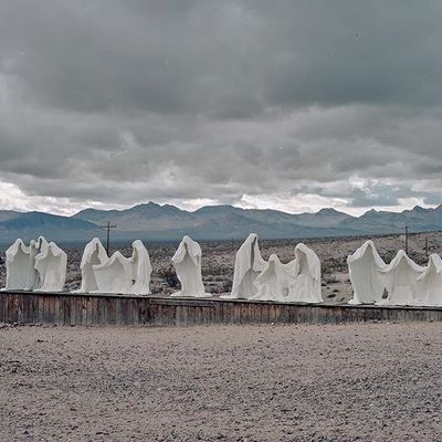 a row of white sculptures sitting on top of a dirt field