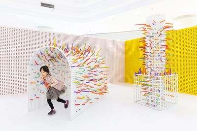 a little girl is walking through a room with colorful sculptures