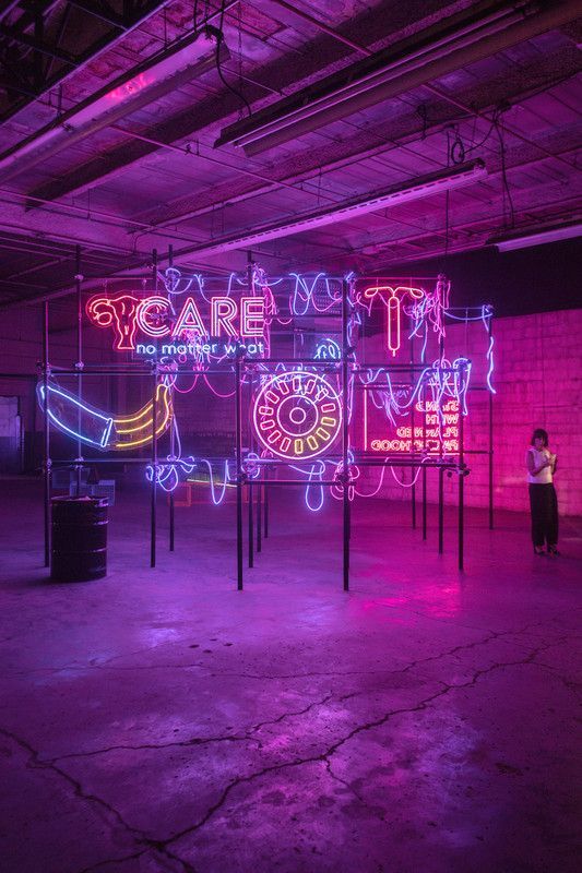 a neon sign in a dark room with a woman standing in front of it