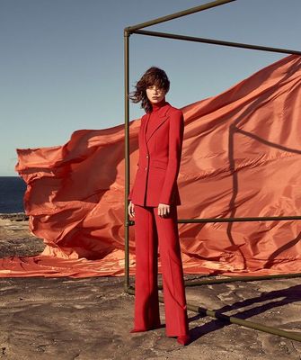 a woman in a red suit standing in front of an orange flag