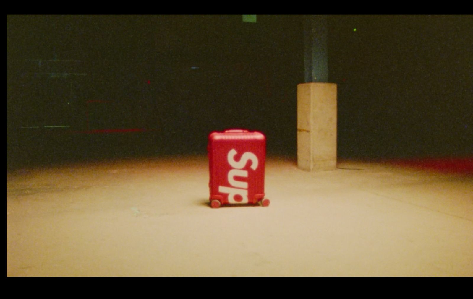 a red suitcase sitting on the ground next to a pole