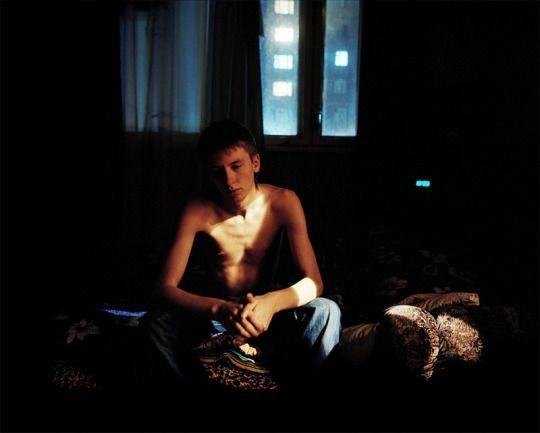 a shirtless man sitting on a bed in a dark room