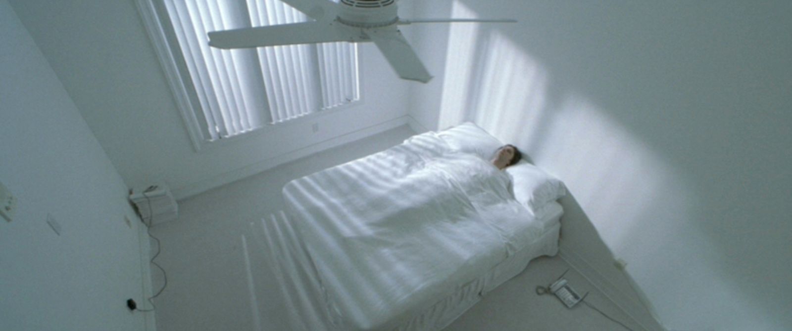 a white bed sitting under a window next to a ceiling fan