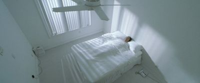 a white bed sitting under a window next to a ceiling fan