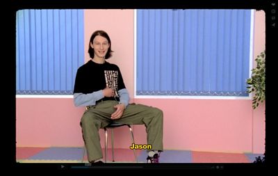 a man sitting on a chair in front of a pink wall