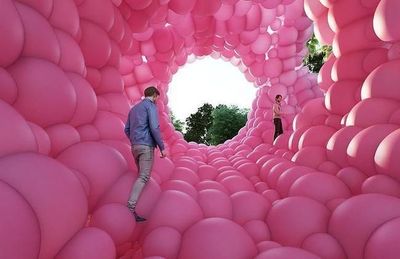 a man walking through a tunnel of pink balloons