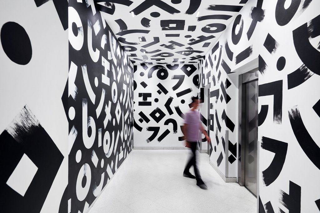 a man walking down a hallway covered in black and white letters