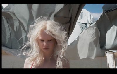 a woman with blonde hair standing in front of an umbrella