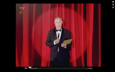 a man in a tuxedo standing in front of a red curtain