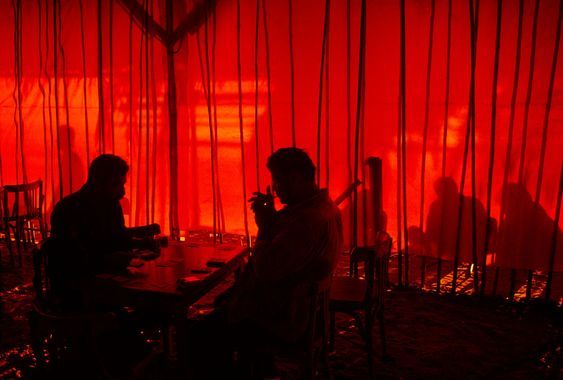 two people sitting at a table in front of a red curtain