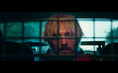 a man with blonde hair behind bars in a cage