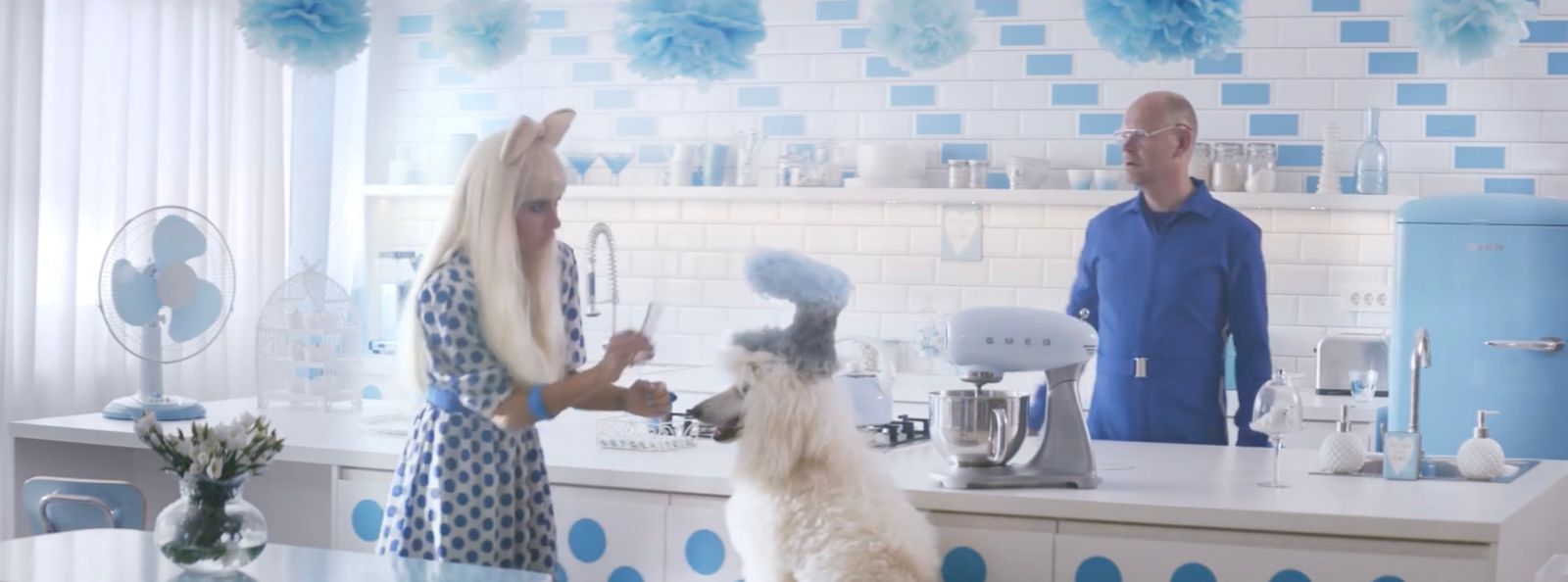 a man and a woman in a kitchen with a dog