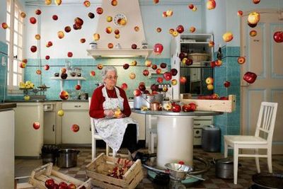 a woman sitting in a kitchen surrounded by apples