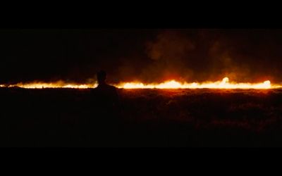 a person sitting in a field with a fire in the background