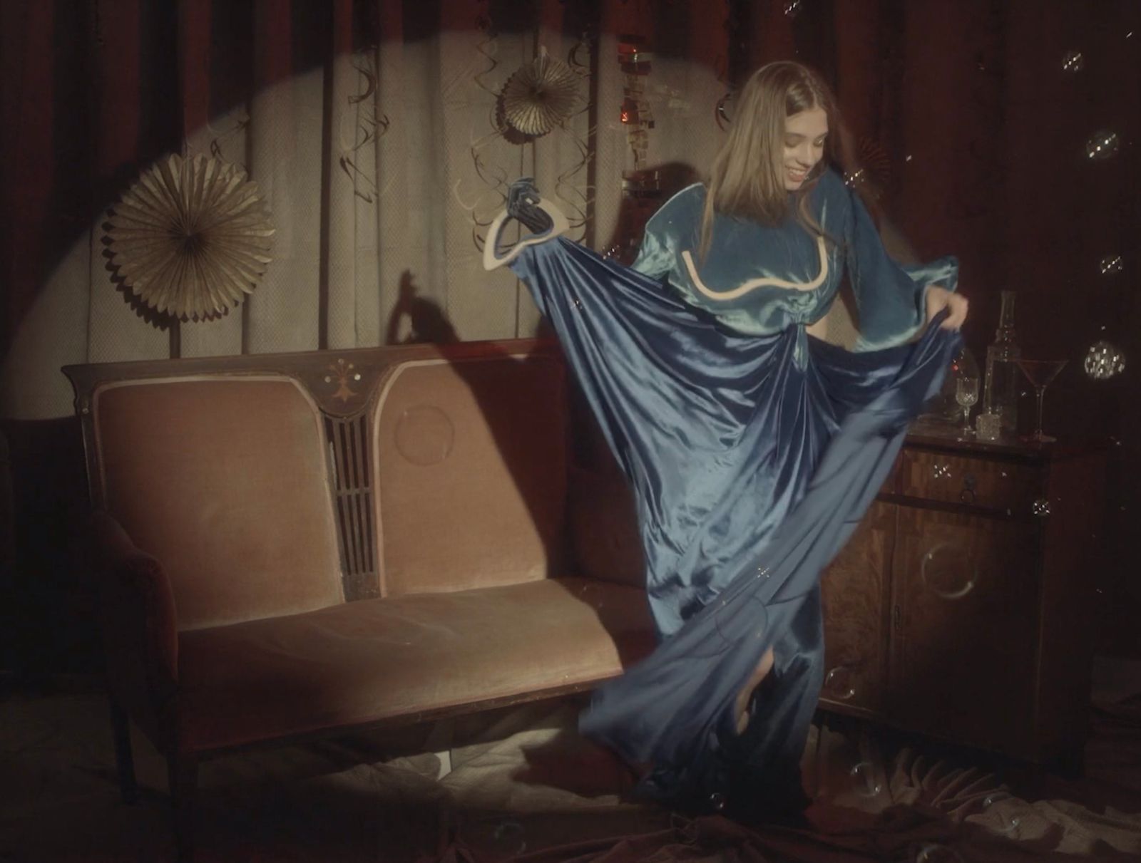 a woman in a long blue dress standing next to a couch