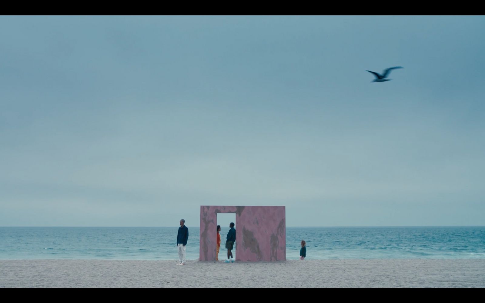 three people standing on a beach looking at the ocean