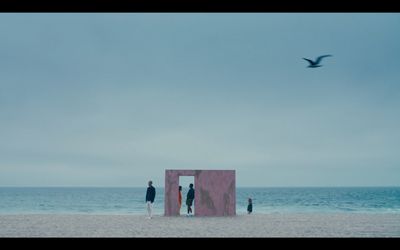 three people standing on a beach looking at the ocean