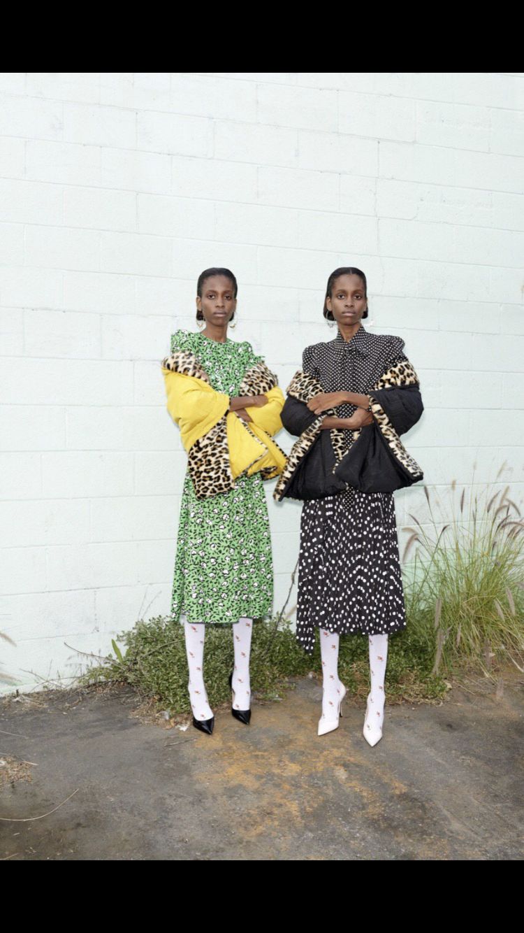 two women standing next to each other in front of a white wall