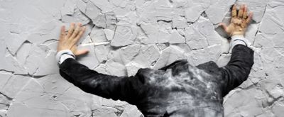 a man in a suit and tie standing in front of a cracked wall