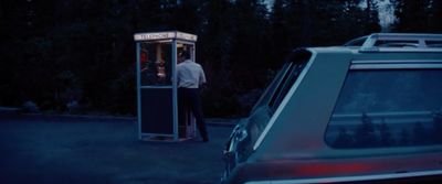 a man standing in a phone booth next to a car