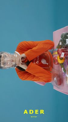 a woman in an orange jacket is holding a plastic bag