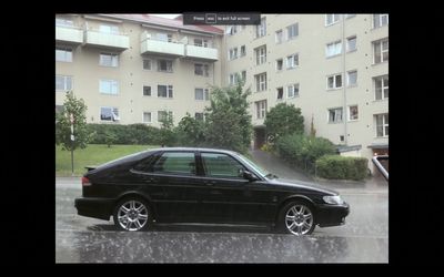 a black car parked in a parking lot in the rain