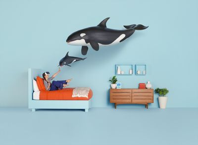 a woman sitting on a bed with an orca whale wall decal above her