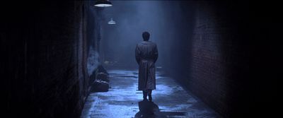 a man in a trench coat standing in a dark alley