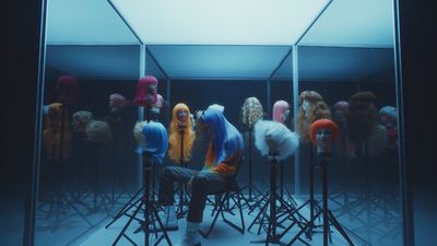 a man sitting in a chair in front of a display of wigs