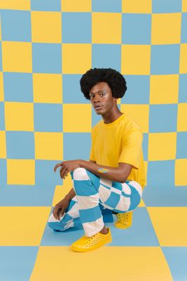 a young man sitting on a checkered floor in a yellow shirt