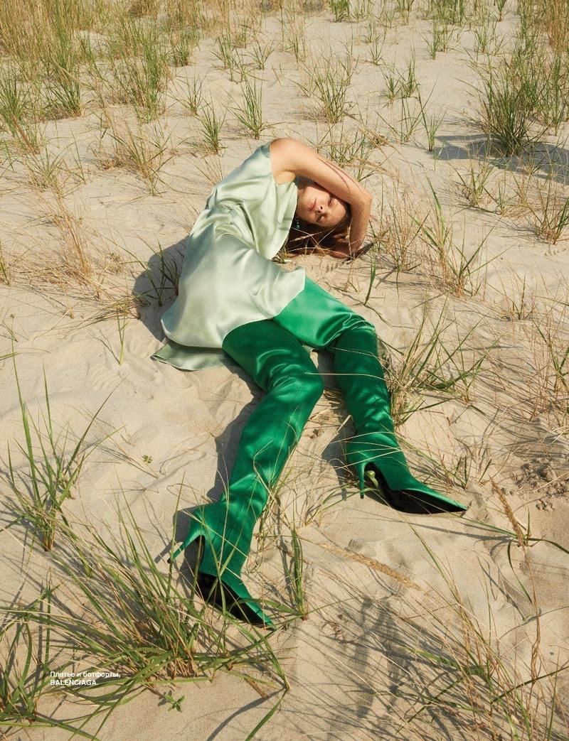 a woman laying in the sand wearing green boots