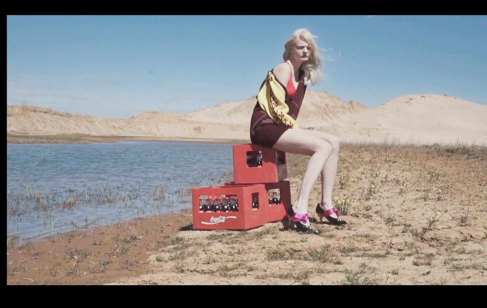 a woman sitting on top of a red box next to a lake