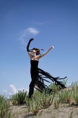 a woman in a black dress is dancing in the sand